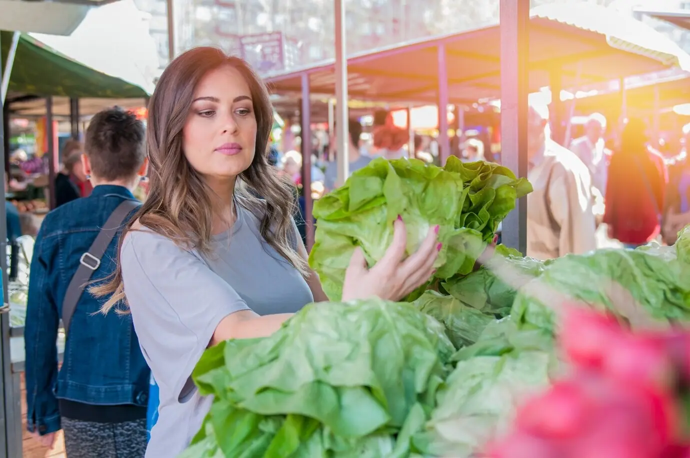Eine Frau kauft Obst und Gemüse auf einem lokalen Lebensmittelmarkt. Marktstand mit einer Vielfalt an Bio-Gemüse. Porträt einer schönen jungen Frau, die grünes Blattgemüse auswählt.